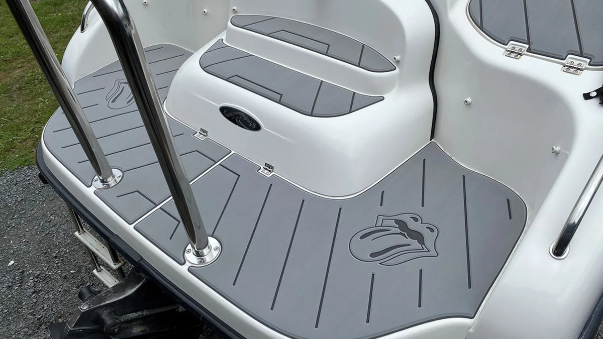 Grey grooved marine deck pads with fitted borders around a seat base, step and stainless steel rail