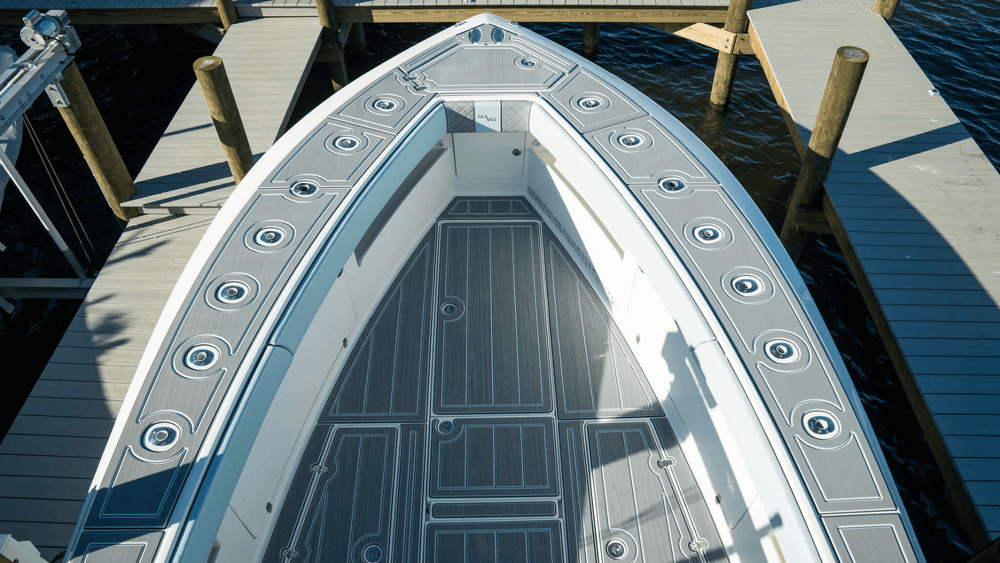 Flat grey boat deck panels with outlined hatches fitted inside a pointed bow beside a marina dock